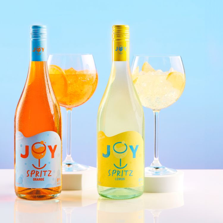 Bottles of two Joy Spritz flavours, Orange and Lemon, with filled glasses behind them and a hue'd blue/pink background.