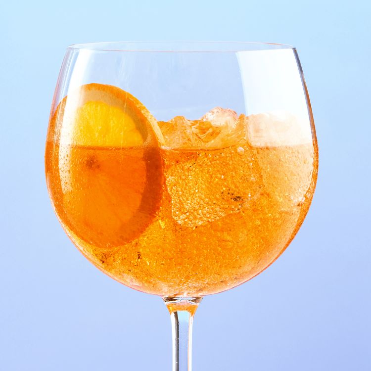 A glass of Joy Spritz Orange flavour with an orange slice and gradient background.