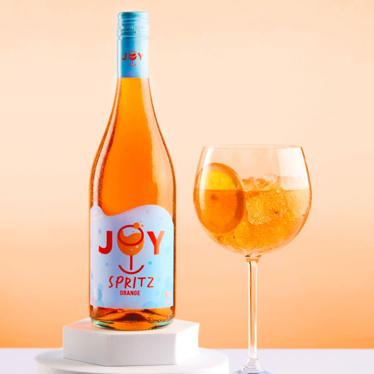 Joy Spritz bottle and glass with an orange gradient background.