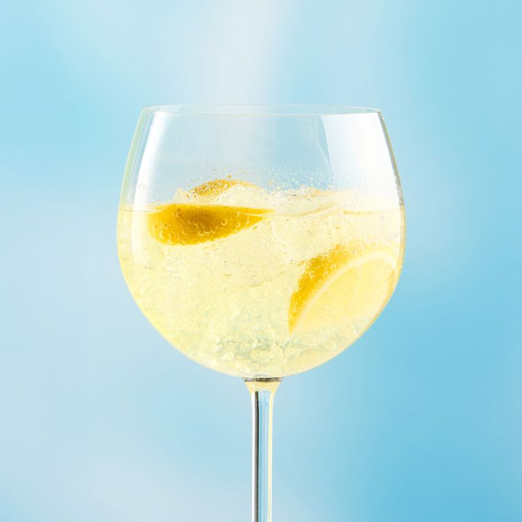 A glass of Joy Spritz Lemon flavor with a slice of lemon, set against a gradient background.